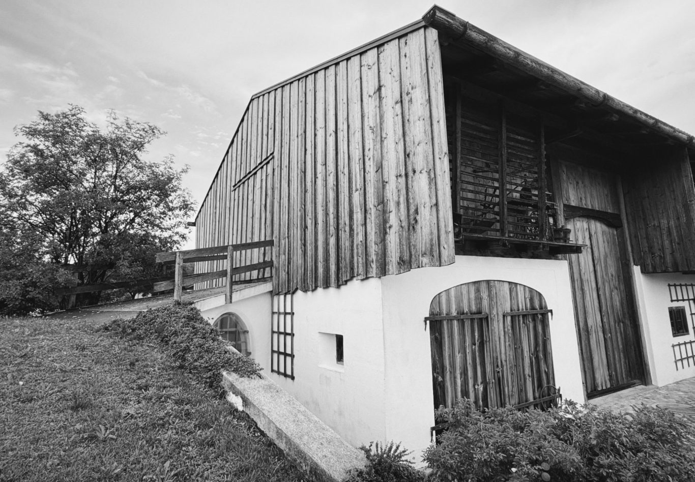 Alter Bauernhof in Schwarz-Weiß mit Holzfassade und weiten Wiesen.